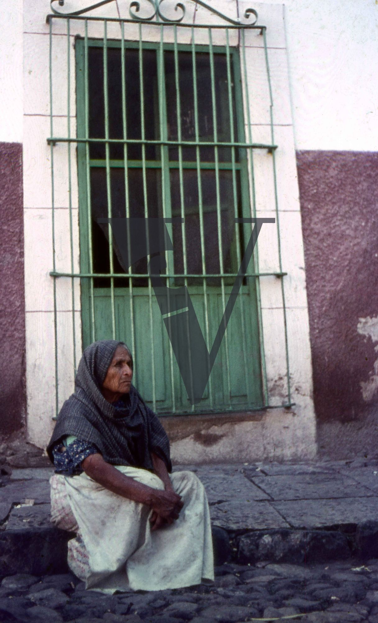 Mexico, Woman in shawls on pavement in front of green winow.
