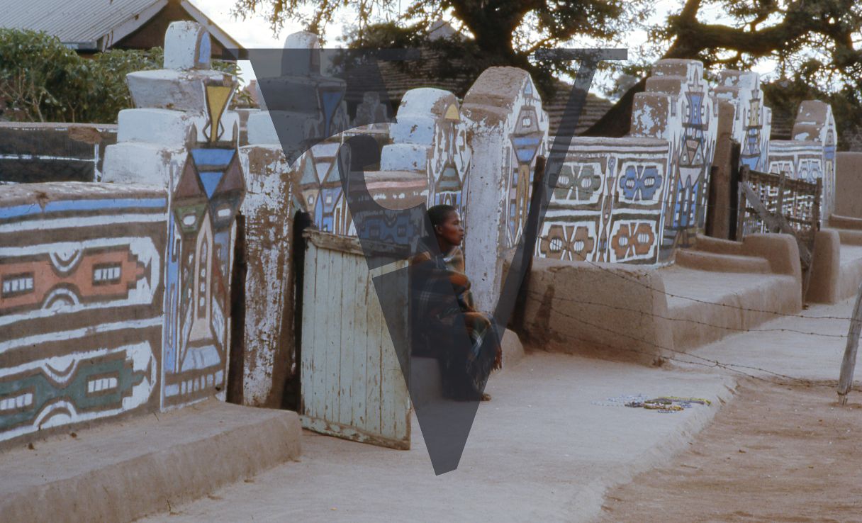 South Africa, Ndebele village, woman sitting next to a painted wall.