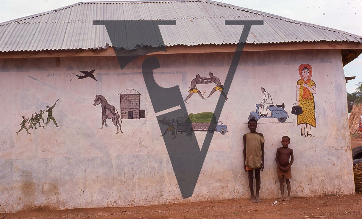 Nigeria, boys in front of folk artwork on building.
