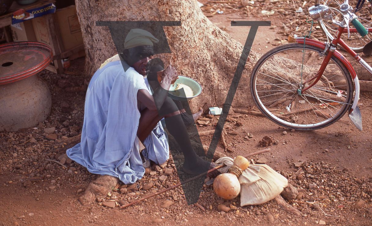 Nigeria, man eating food by red bicycle.