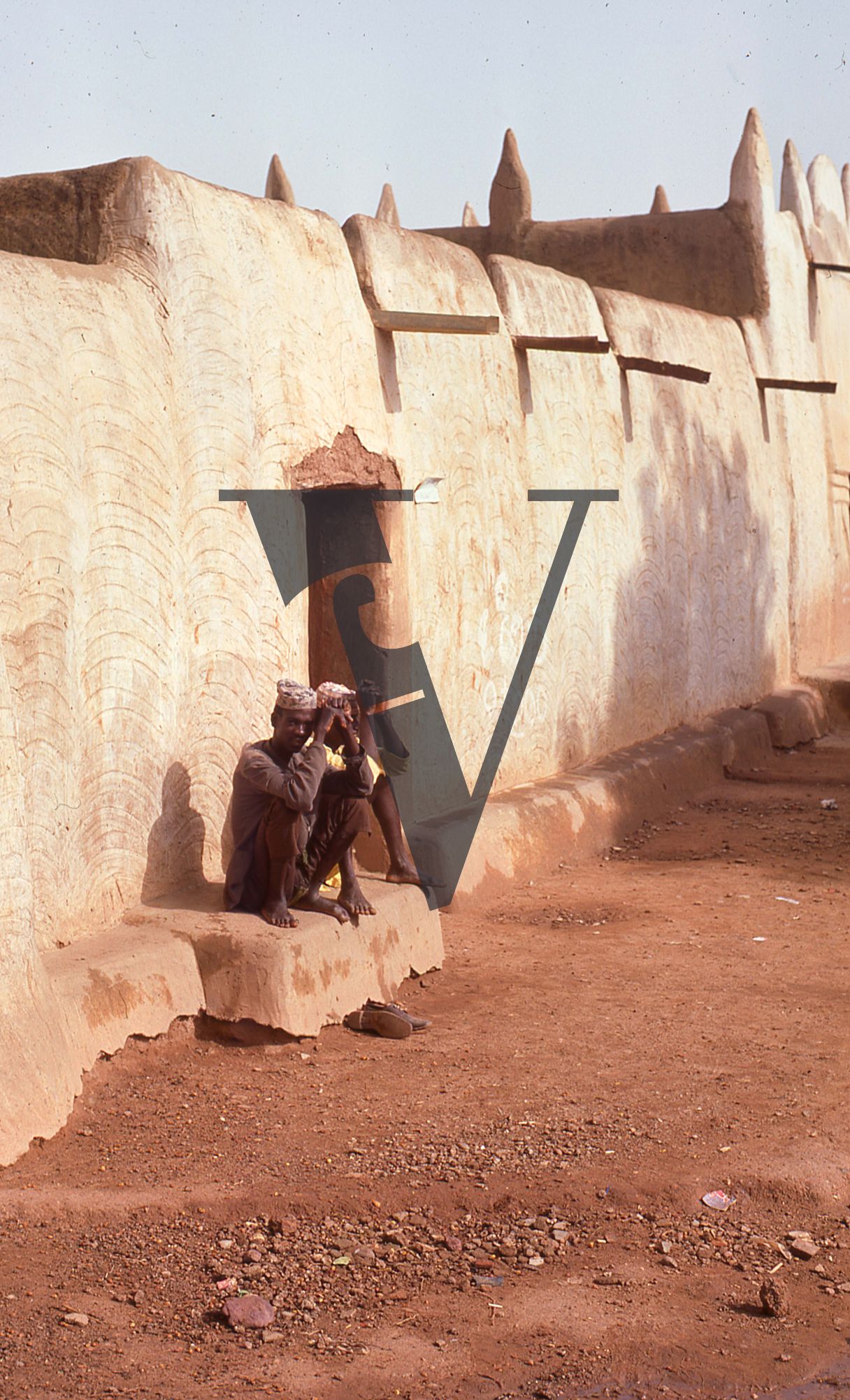 Nigeria, two men seated at base of wall.