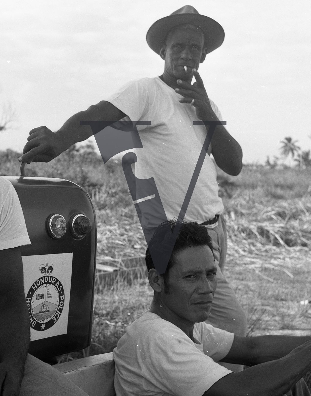Belize, Portrait, men stand by British Honduras Police vehicle, smoking.