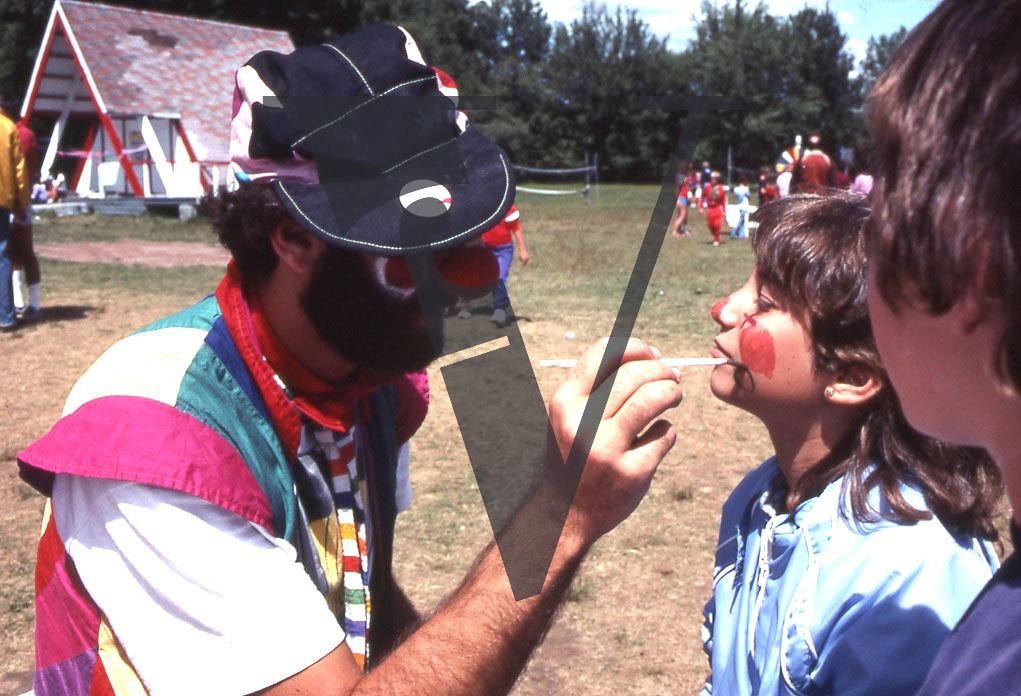Summer camp, man face painting two children.