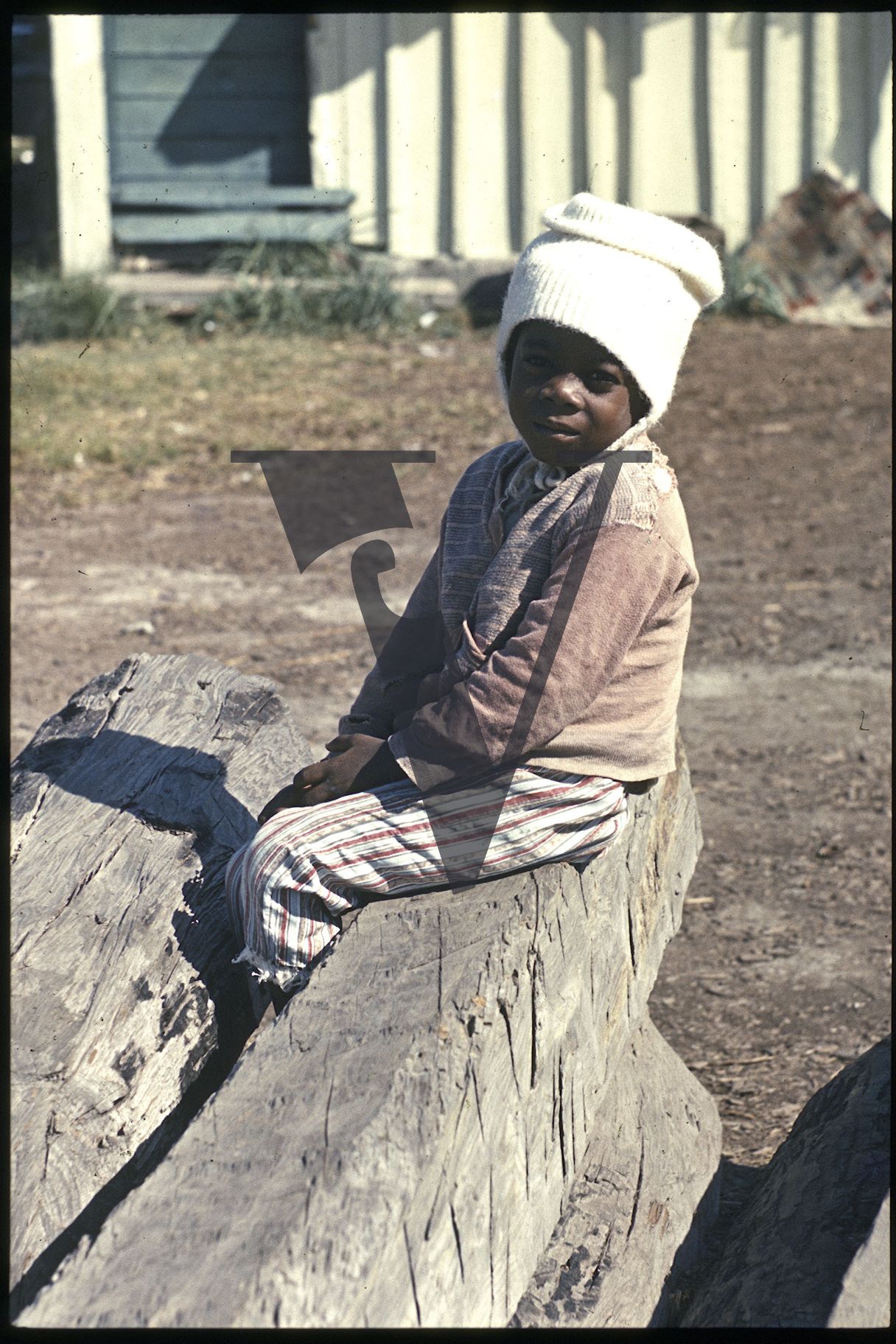 Belize, Boy with hat on, sits on log.