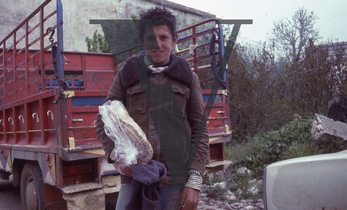 Lebanon, South of Beirut, boy in brown coat stands next to a lorry, holding flatbreads, portrait.