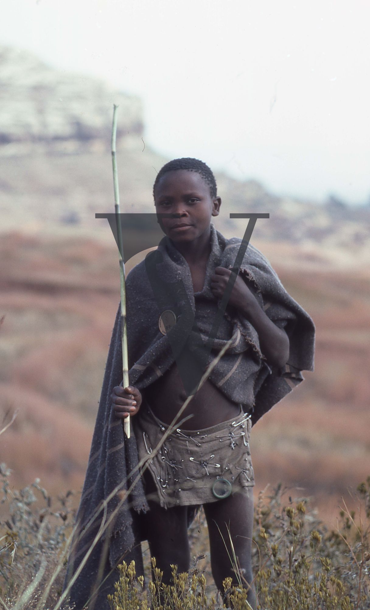 Lesotho, boy with blanket and stick, safety pin shorts, portrait.
