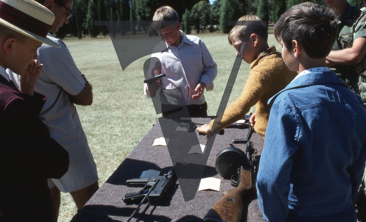 Rhodesia, Salisbury, Rhodesian Light Infantry passing out ceremony, young boys looking at guns on a table, mid-shot.