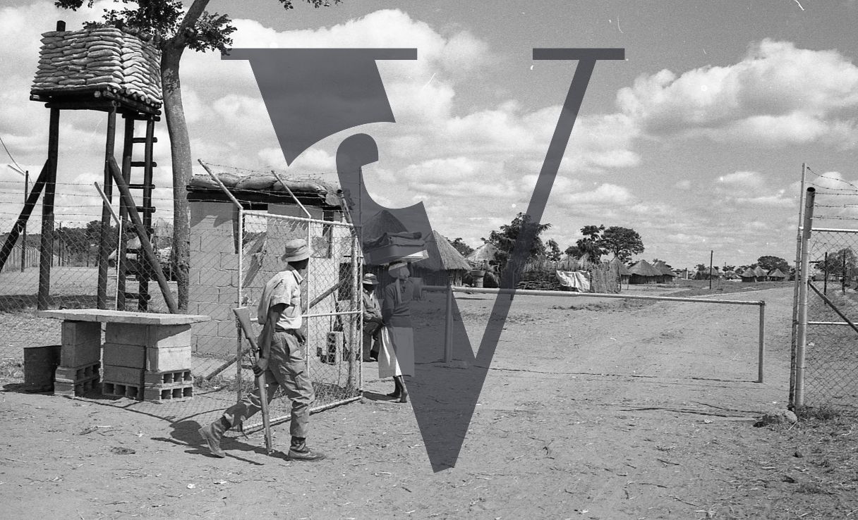 Rhodesia, “protected village”, fence, gun tower, guard with rifle, women, wide shot.