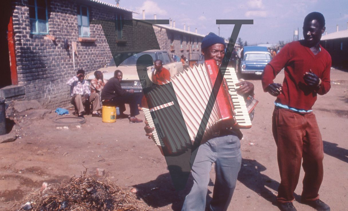 South Africa, Soweto, township, accordion player, dancer, jovial, onlookers, cars.