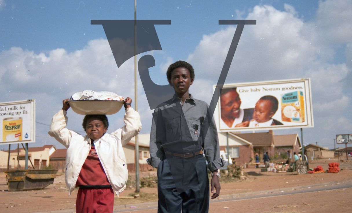 South Africa, township, two children, carrying laundry, billboards, portrait.