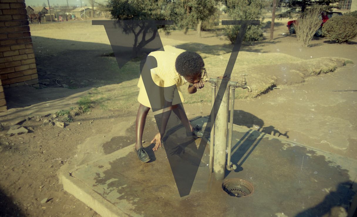 South Africa, Soweto, girl drinking from water pump, exterior.
