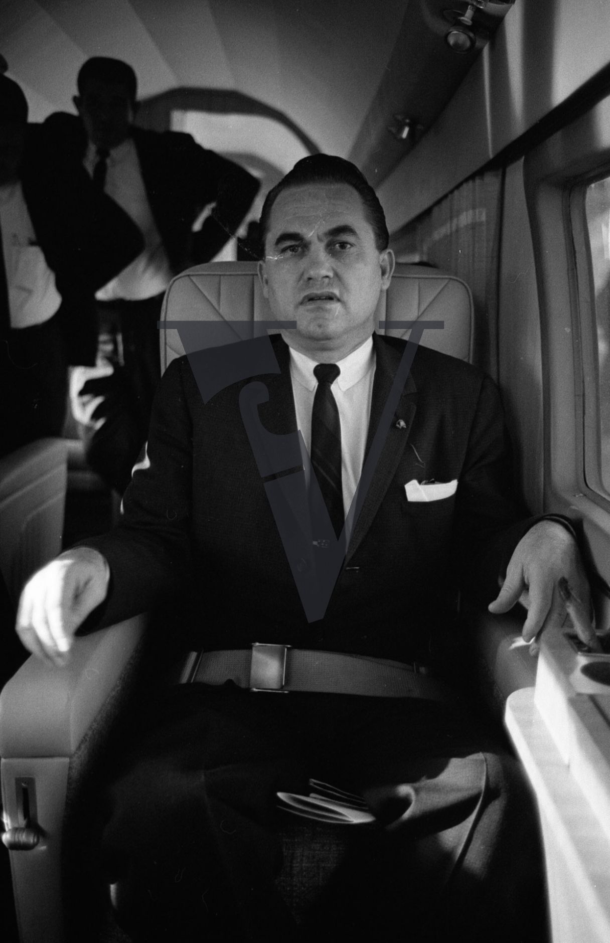 Governor George Wallace, on board plane, scowling.
