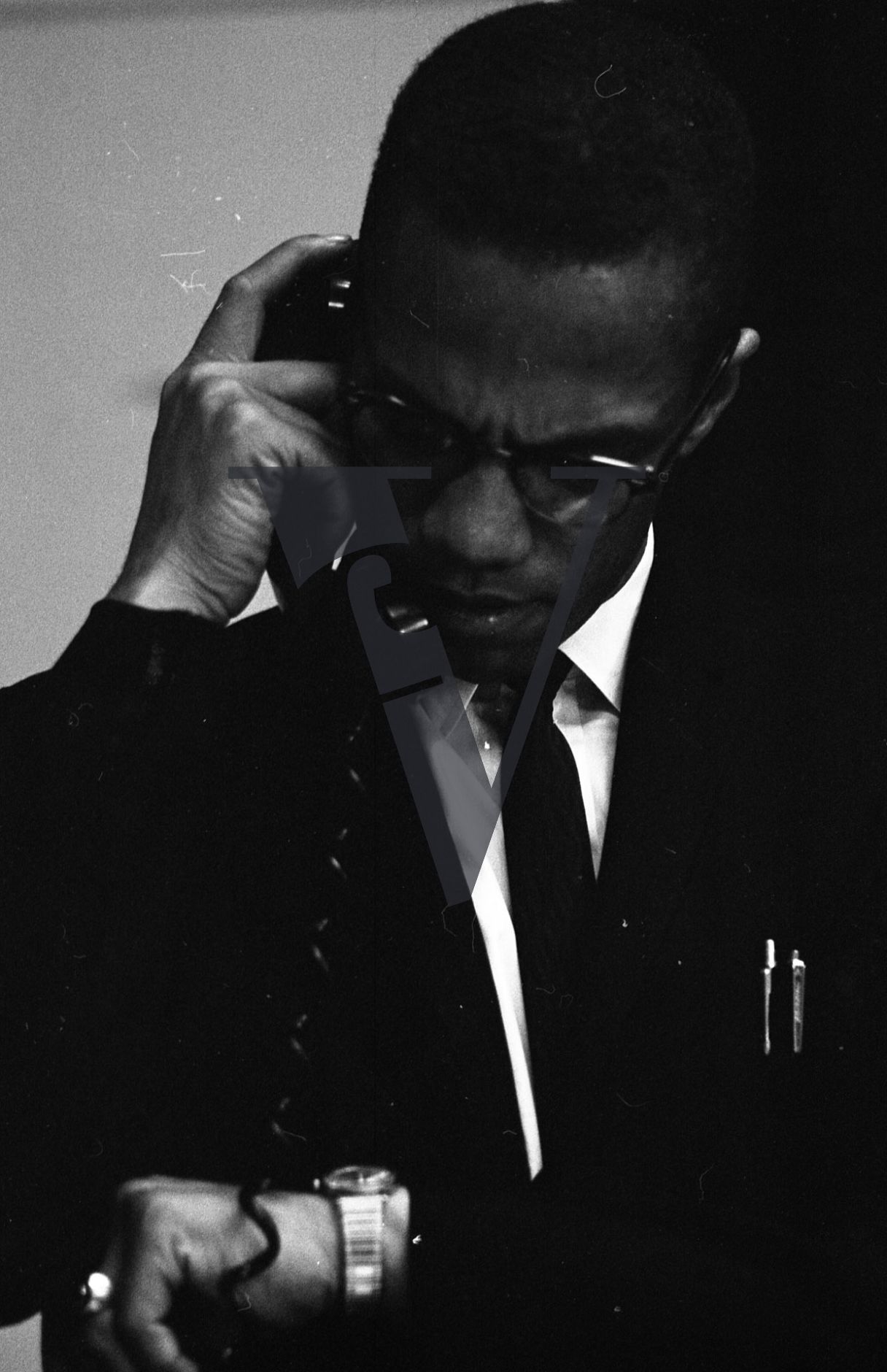 Malcolm X, portrait, on telephone, looking at watch.