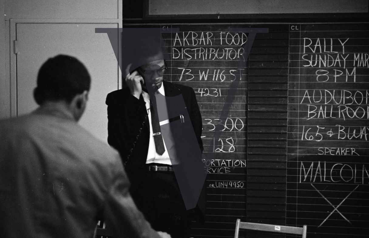 Malcolm X, portrait, on telephone, blackboard behind, Akbar Food distributor.